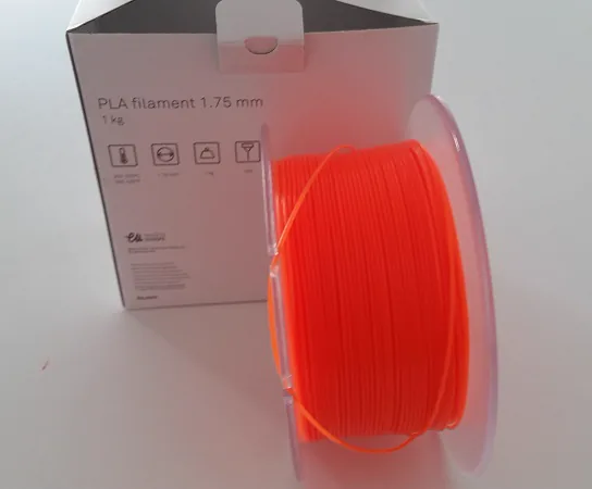 Szpula pomarańczowego filamentu PLA o średnicy 1,75 mm na tle kartonowego opakowania