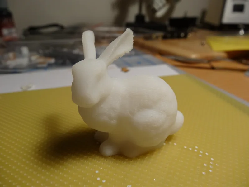 Biały wydruk królika Stanford Bunny po usunięciu podpór i raftu, z drobnymi resztkami materiału na podkładce obok